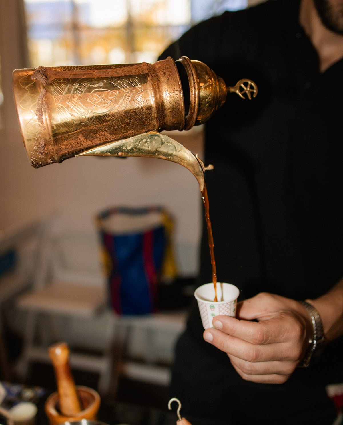 Coffee being poured from a traditional brass pot into a guest's cup at a Dunes gathering