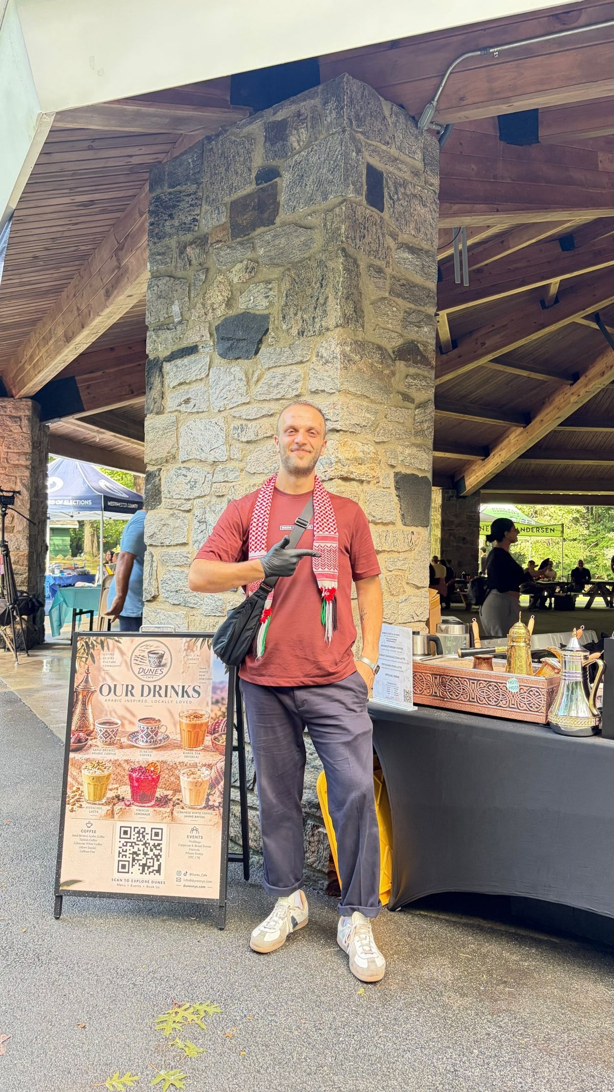 A person beside the Dunes drinks menu and traditional coffee service at an outdoor gathering